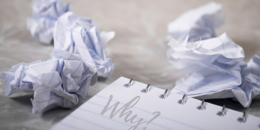 Crumpled paper next to a notepad with the word "Why?"